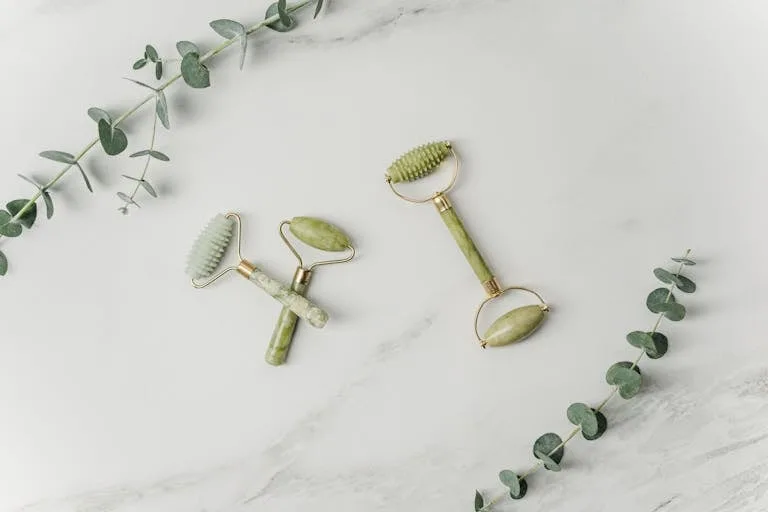 Elegant jade facial rollers and eucalyptus leaves on marble surface, promoting a spa-like ambiance.