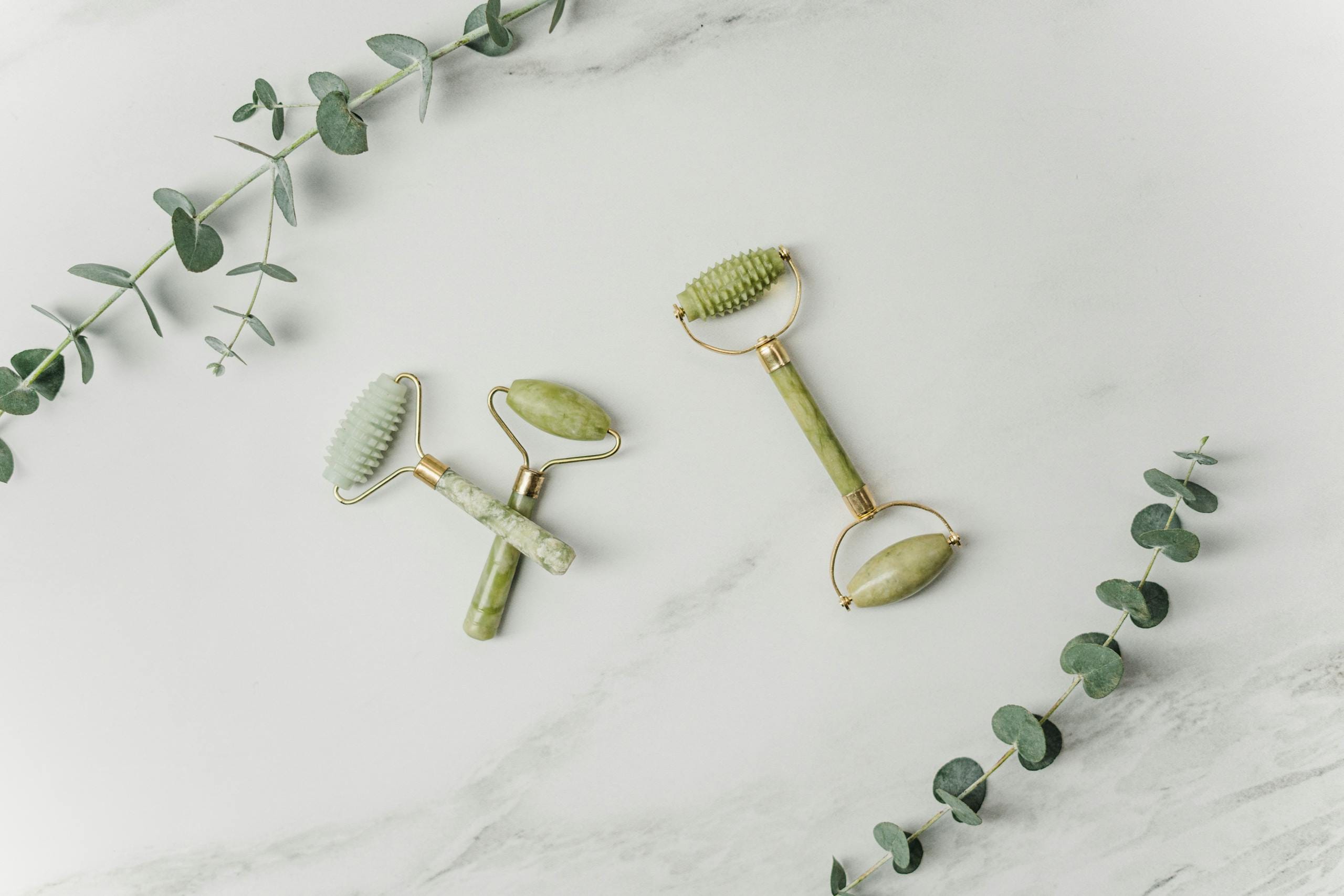 Elegant jade facial rollers and eucalyptus leaves on marble surface, promoting a spa-like ambiance.